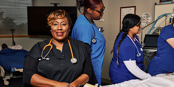 Image of a respiratory therapy instructor smiles in front of a scene where students are practicing on a mannequin.